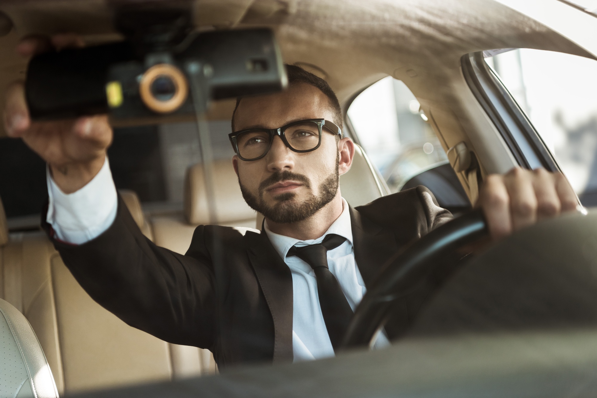 beau chauffeur en costume conduisant une voiture et fixant un miroir