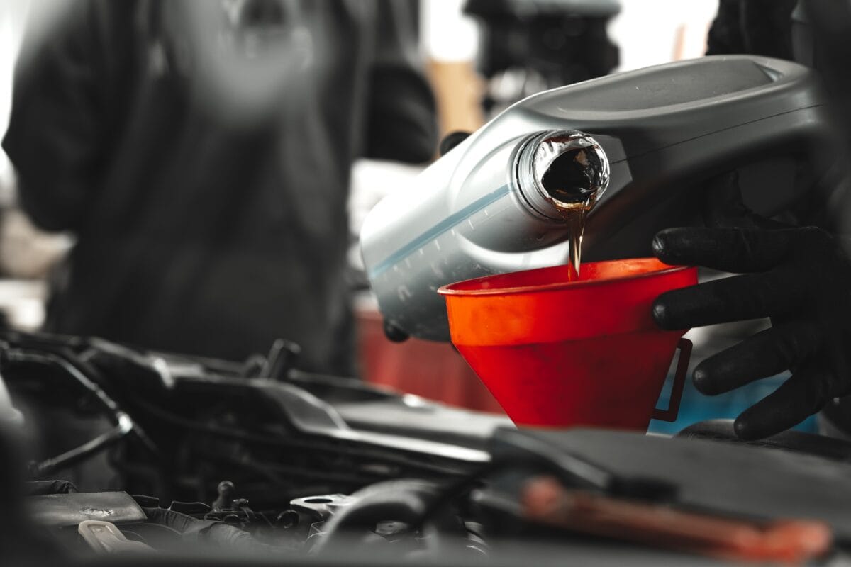 Gros plan d'un technicien automobile versant de l'huile neuve dans le moteur de la voiture