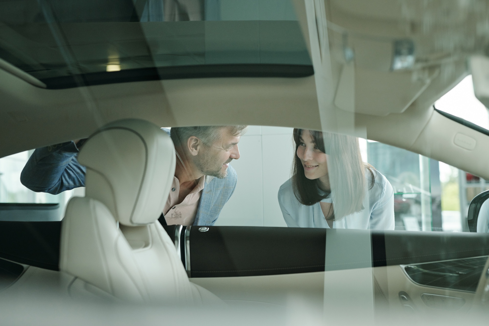 Des clients heureux se tiennent près d'une voiture dans un centre automobile et se penchent vers la fenêtre.