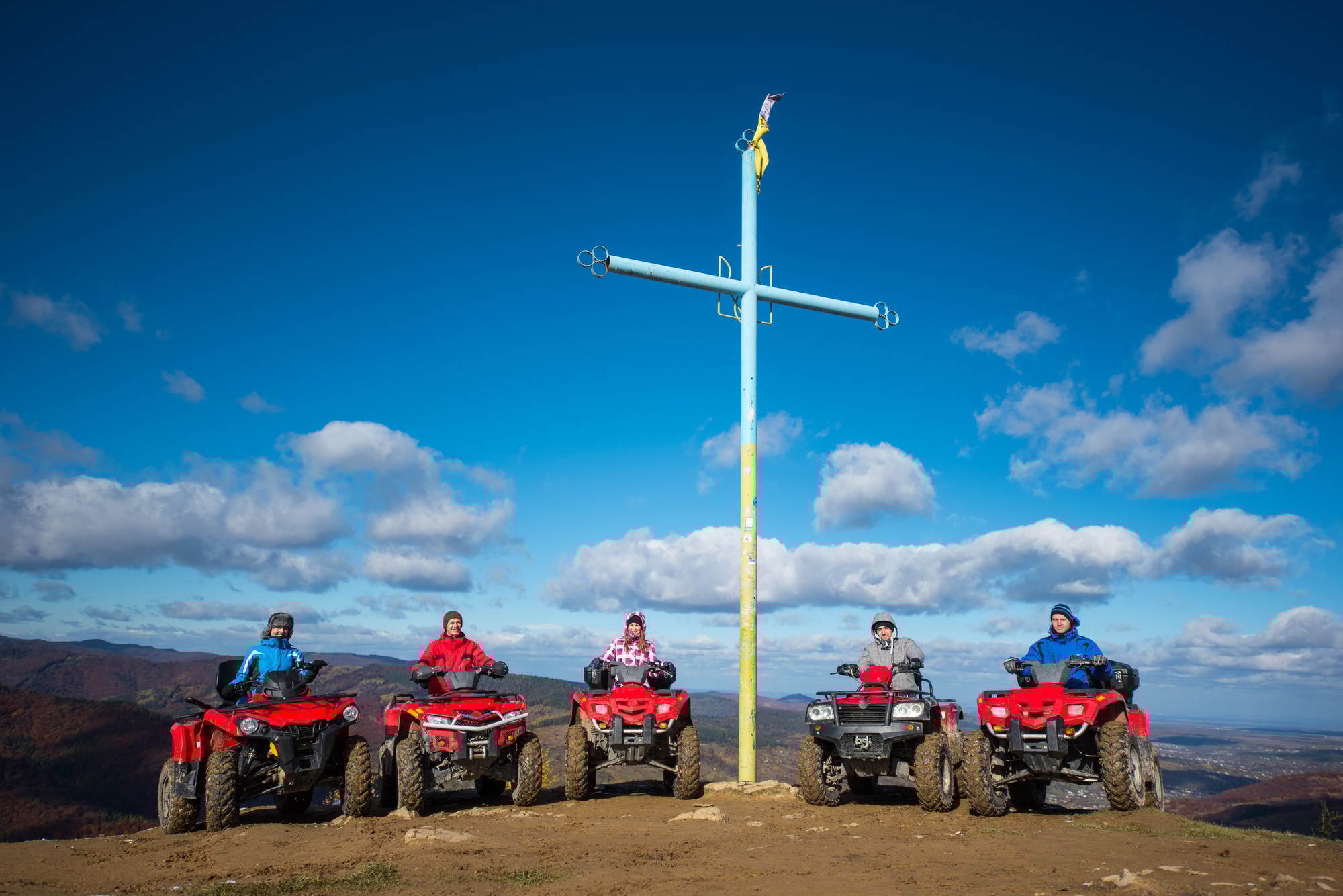 Groupe de personnes sur des quads rouges près d'une croix avec un symbole de l'Ukraine au sommet de la montagne.