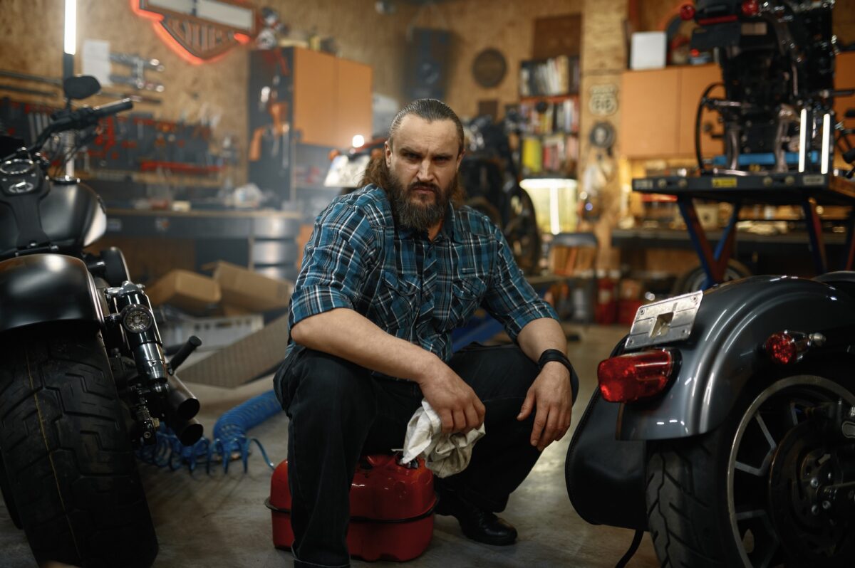 Bearded mature man biker cleaning motorcycle in garage workstation