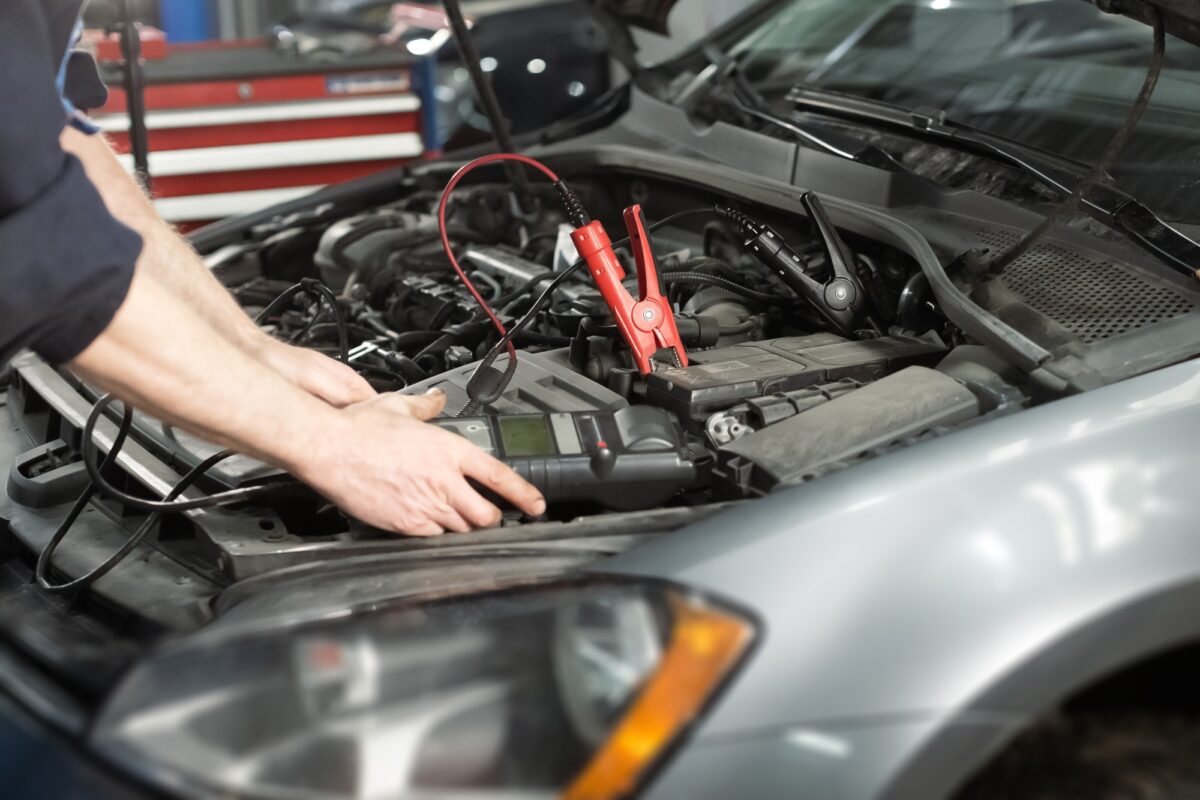 Homme tenant un appareil moderne et vérifiant la tension d'une batterie d'automobile.