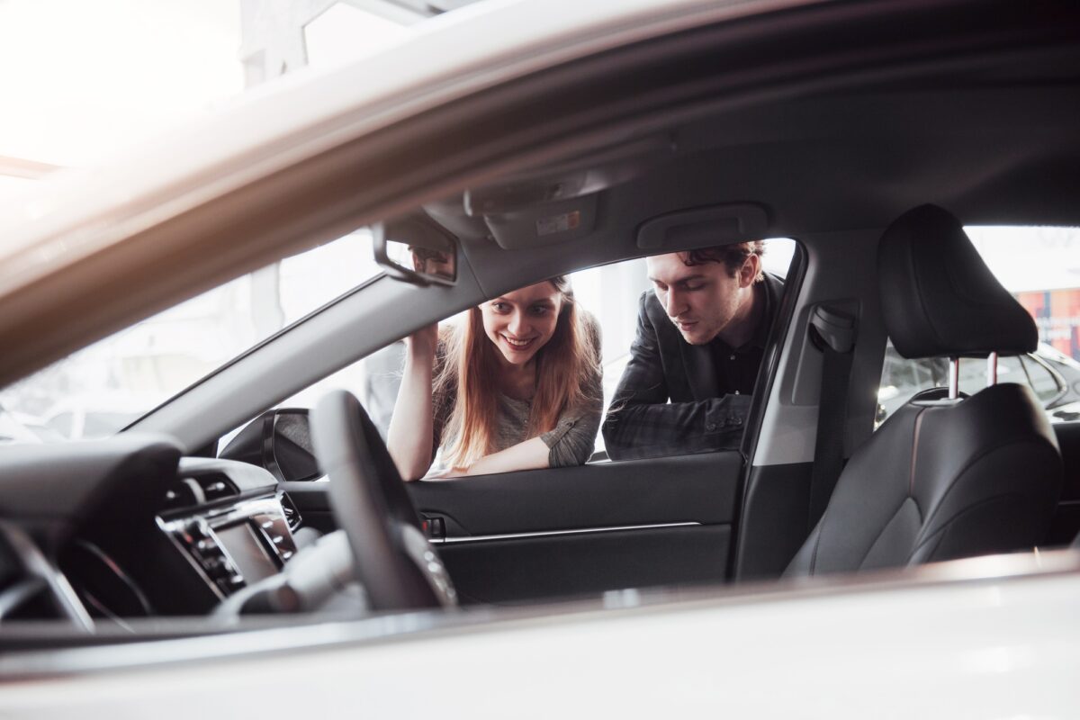 J'aime cette voiture. Un beau jeune couple se tient devant le concessionnaire pour choisir la voiture qu'il va acheter.