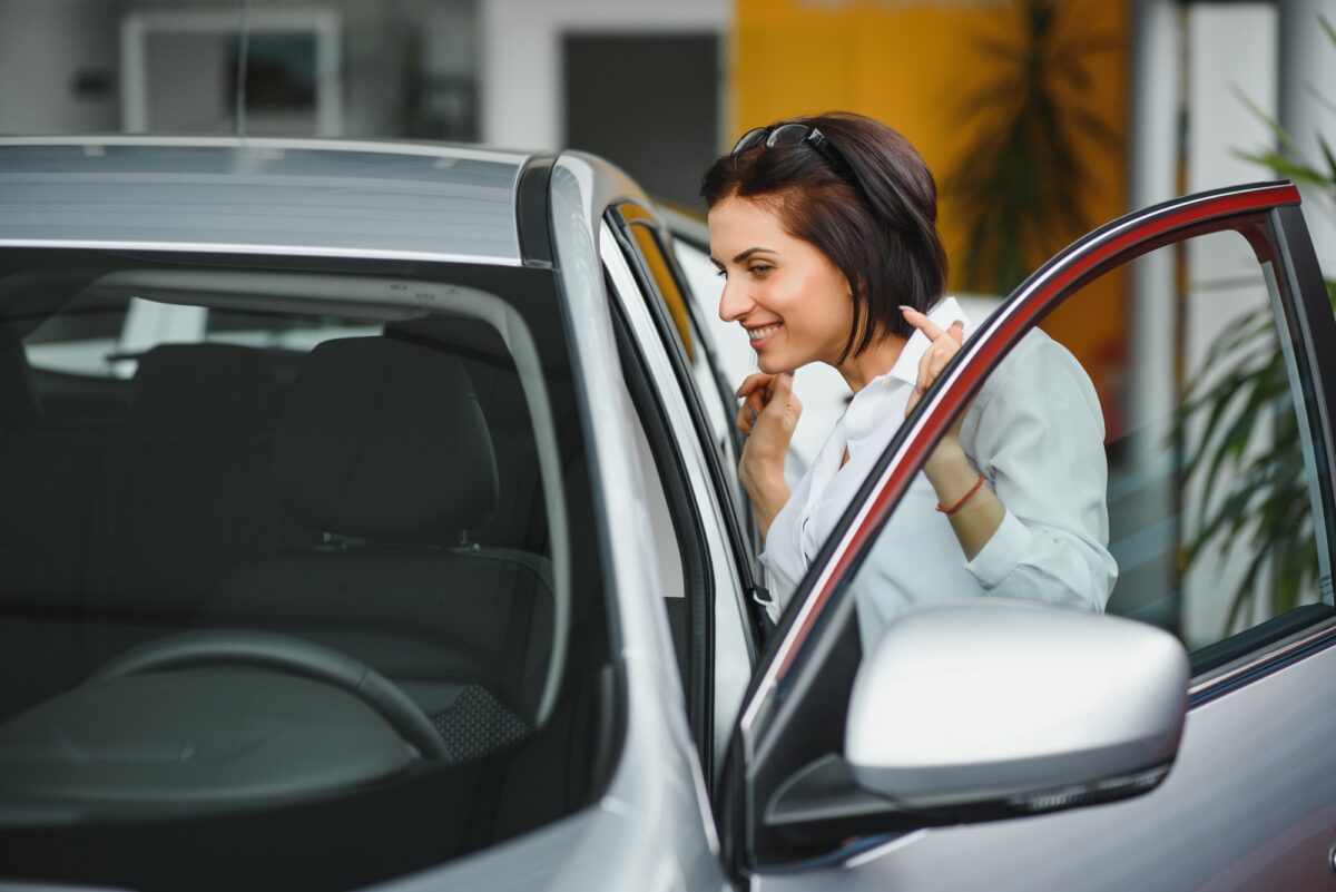 Jeune fille rêvant d'une nouvelle voiture inspectant une nouvelle voiture blanche chez un concessionnaire automobile