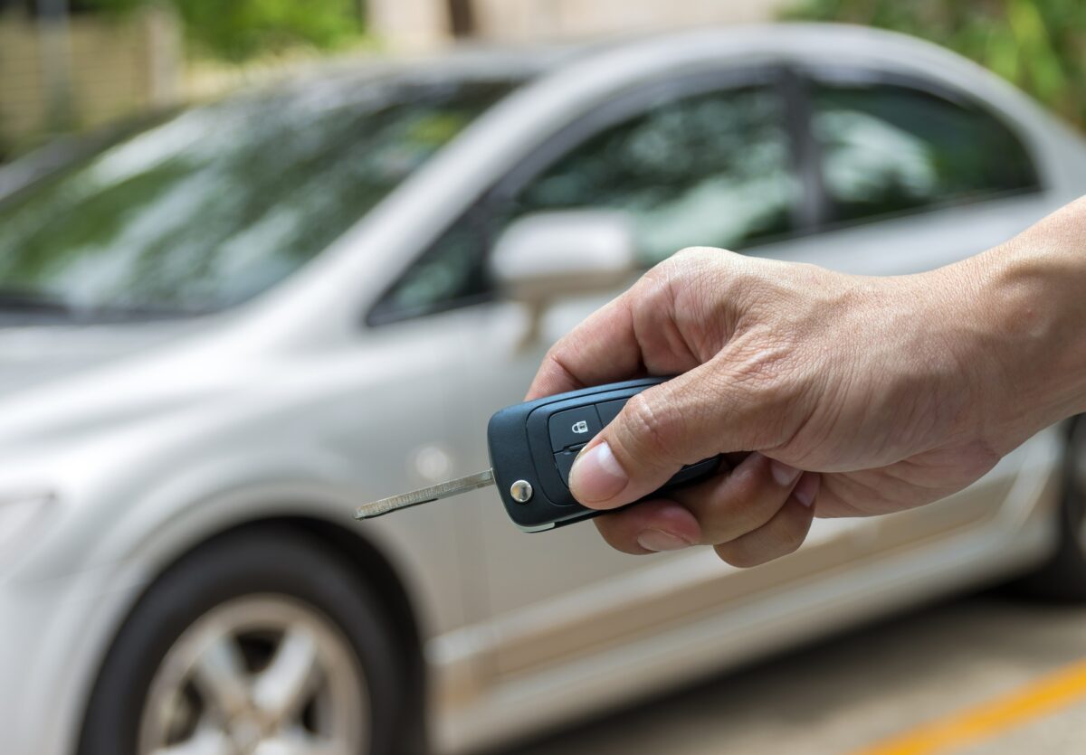 La main tenant les clés sur la photo floue d'une voiture d'occasion pour l'ouverture de la porte de la voiture,