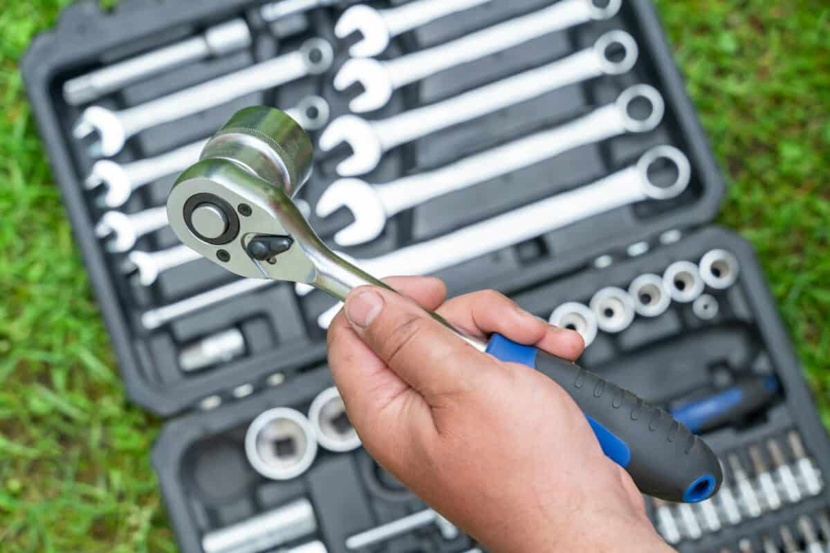 Man's hand holds a metal tool over a box with a set of tools supplies for construction work closeup