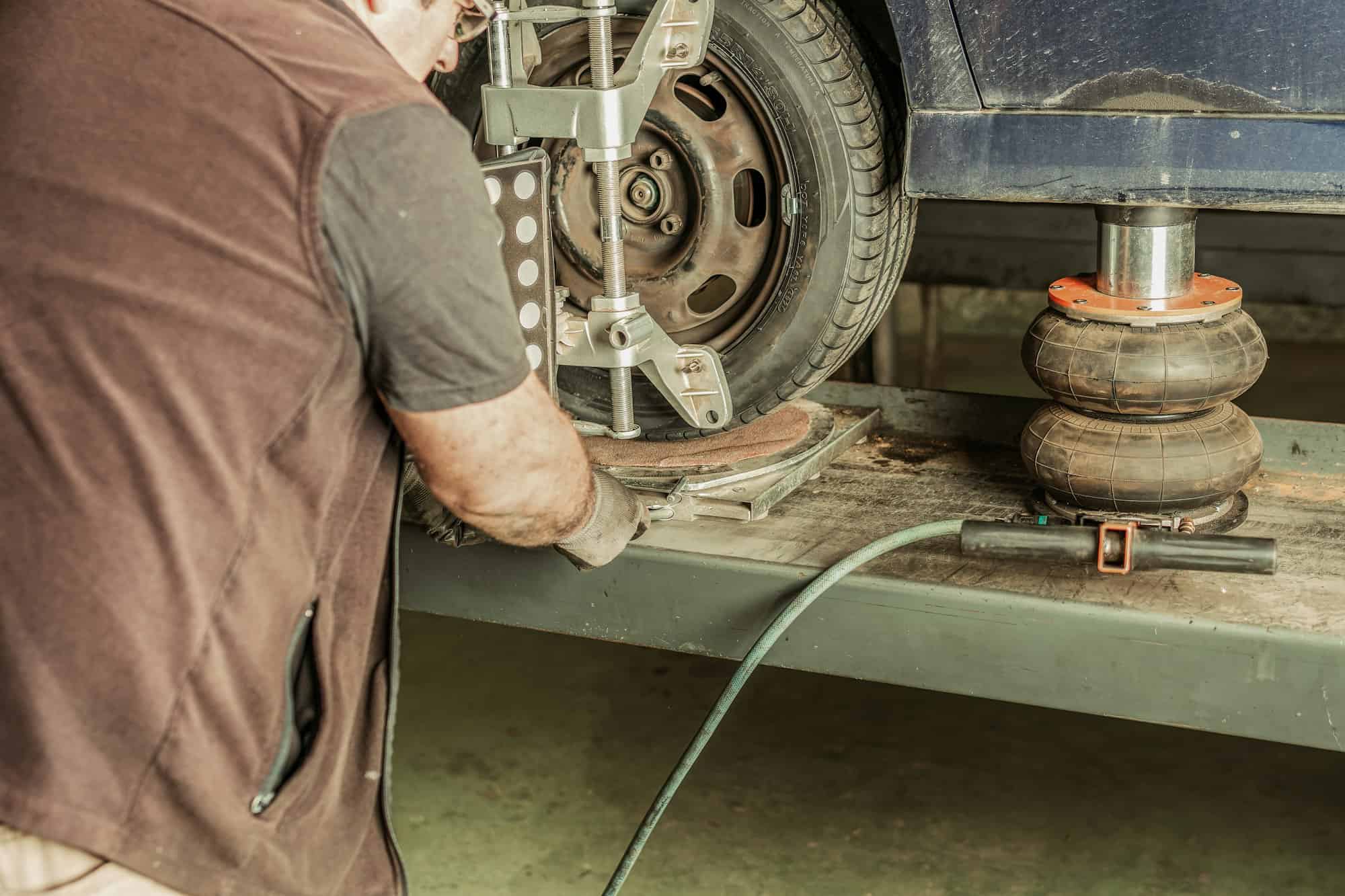 Mechanic aligning the steering of a car lifted by a jack in a garage