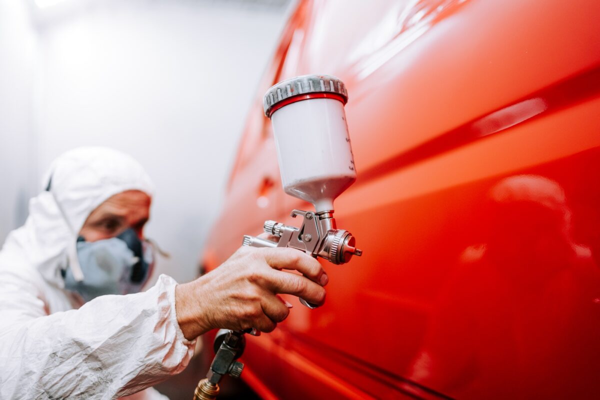 orateur en train de peindre une voiture dans une boîte de peinture spéciale, portant un costume complet