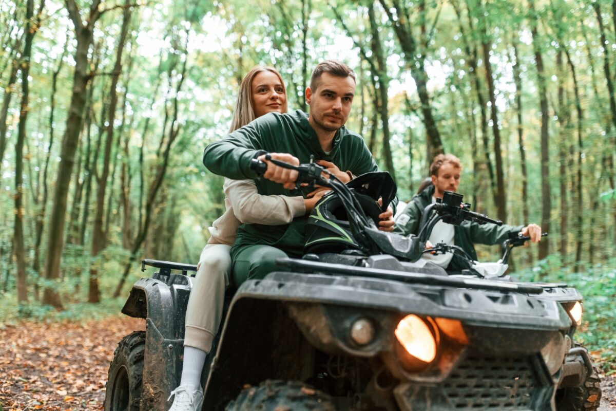 Riding and smiling. Young couple riding a quad bike in the forest