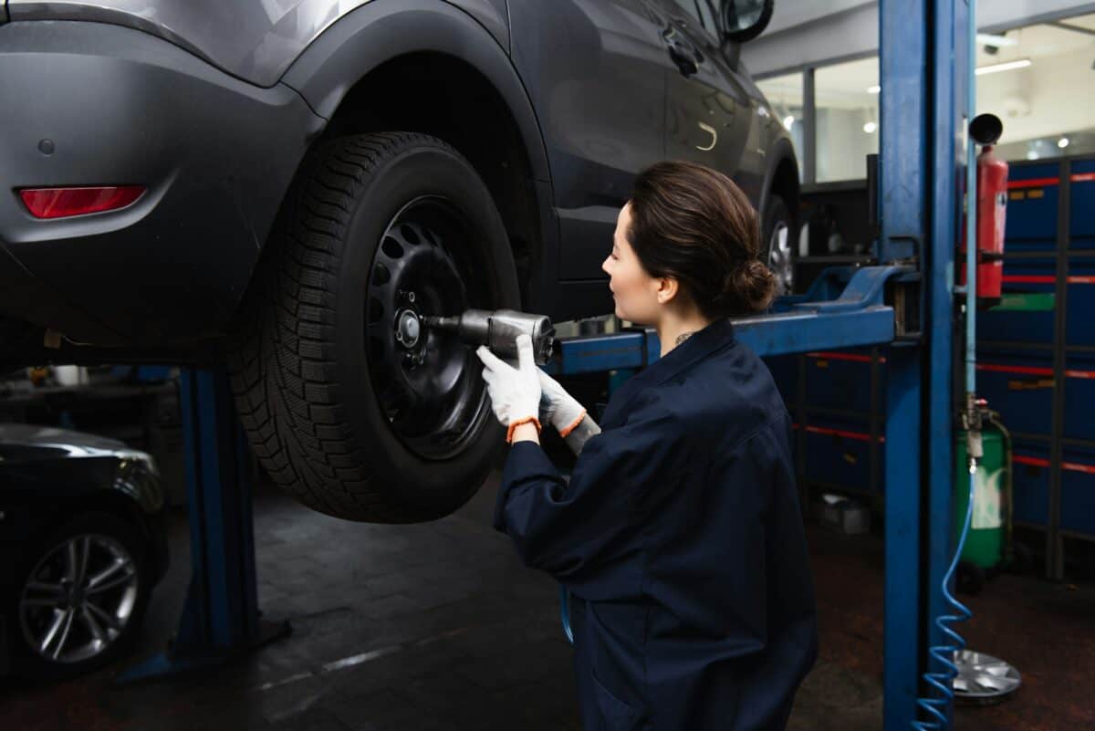Side view of forewoman working with impact wrench on wheel of car in service