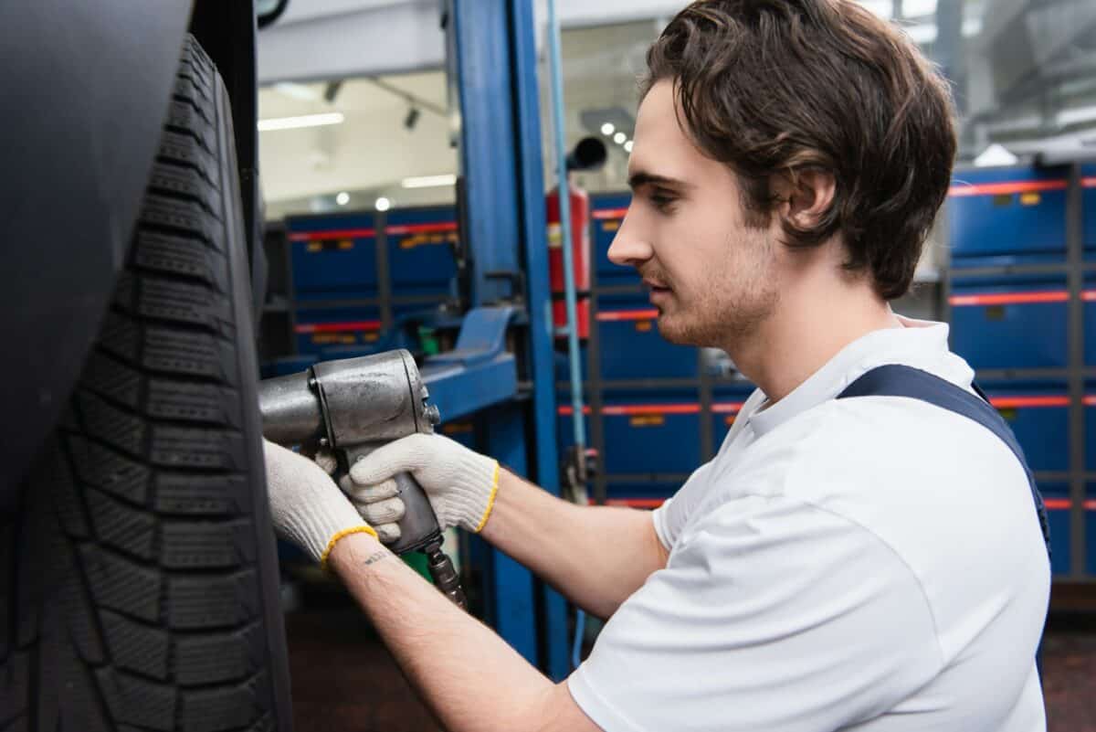 Side view of mechanic working with impact wrench on car wheel in garage
