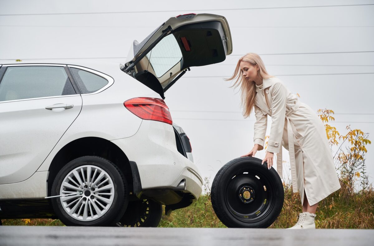 Une fille roule une roue de secours pour la remplacer près de sa voiture.