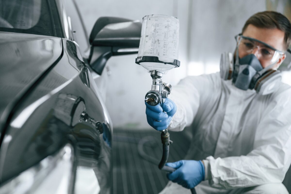 Vêtements de protection blancs. Un homme peint une voiture à l'aide d'un spray.