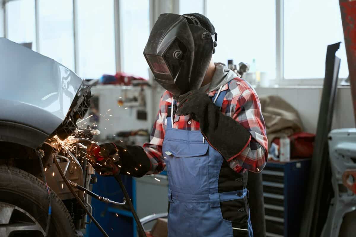 Welder in work overalls works in a car workshop